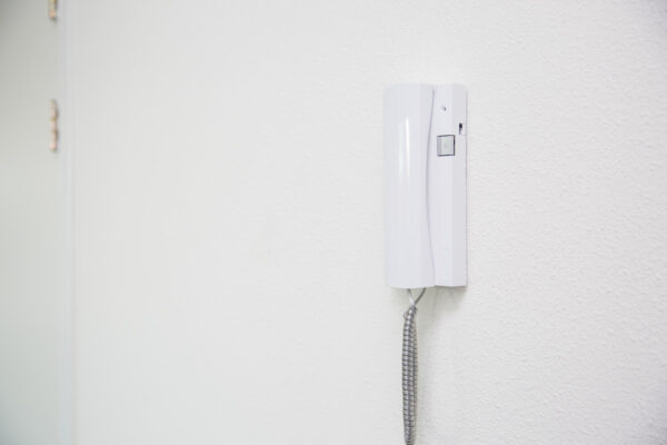 Witte intercom aan de muur in een helder verlichte gang op de Laan van ’s-Gravenmade.